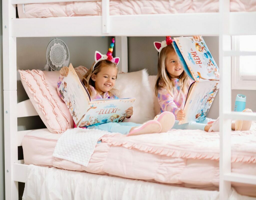 Two girls sitting on the bed and reading Hooray Heroes' personalised birthday books.